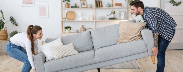 A woman and man are moving a sofa in their living room