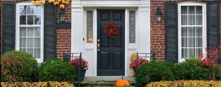 image shows the front door and 2 adjacent windows of a house decorated for the fall season