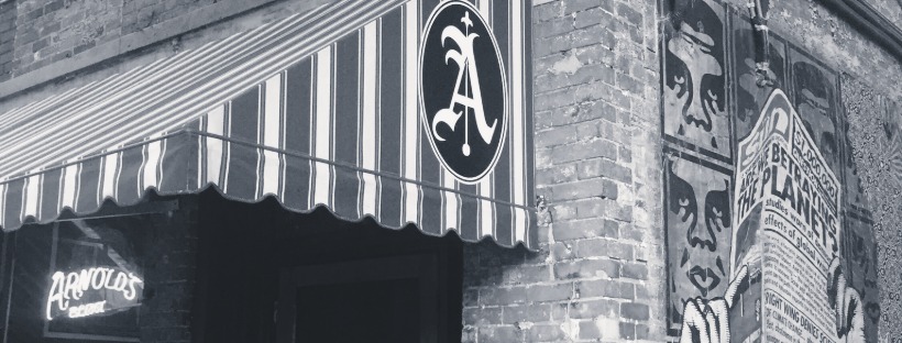 Arnold’s Bar & Grill brick storefront with striped awning and round “A” sign in Over-the-Rhine.
