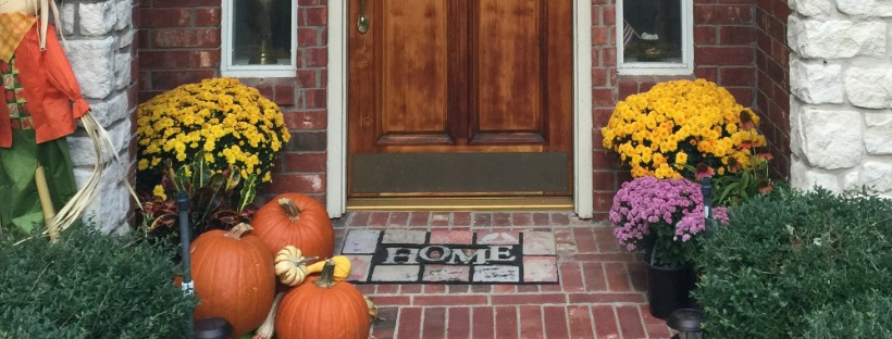 Home entry with a doormat, potted mums and pumpkins—clean, welcoming front door setup.