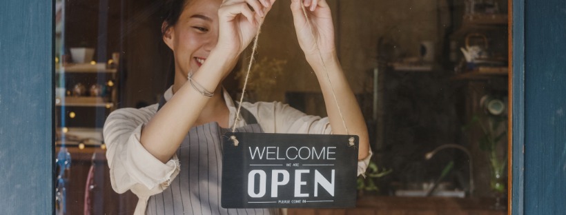 A local small-business owner hangs an “Open” sign on her shop door, symbolizing community support on Small Business Saturday.